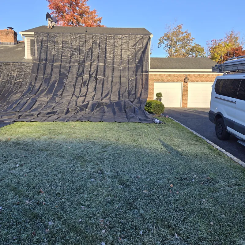 Roof tarped for weatherproofing during a re-roof, autumn foliage in the background
