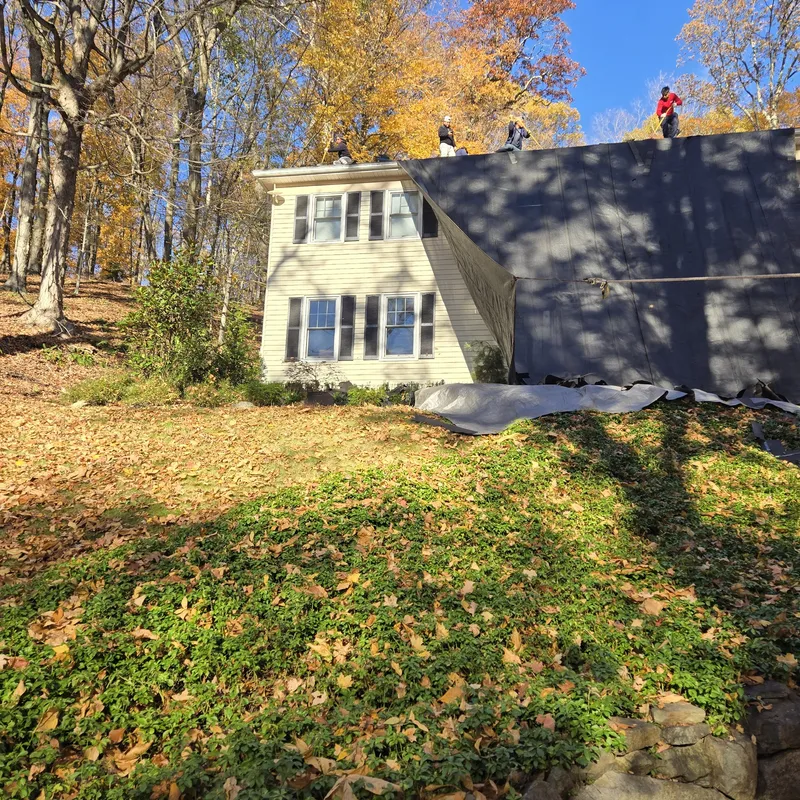 Home with newly installed dark architectural shingle roof, stone retaining wall, fall foliage